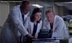 Three doctors in white lab coats closely examine medical images on a monitor in a hospital setting.