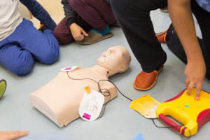 People practice CPR and AED use on a training manikin during a first aid class.