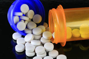Two prescription pill bottles, one blue and one orange, tipped over with white tablets spilling out onto a black surface.