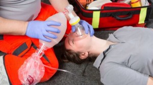 Person performing CPR chest compressions on a training manikin with an automated external defibrillator (AED) in use during a first aid training session.