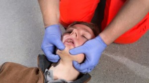 Person performing CPR chest compressions on a training manikin with an automated external defibrillator (AED) in use during a first aid training session.