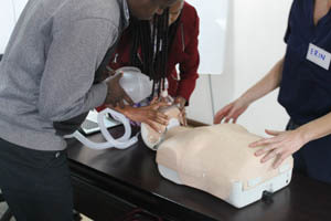 Three people practicing CPR and using a resuscitation bag on a medical training mannequin placed on a table.