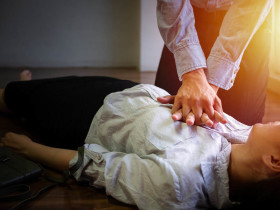 Person performing chest compressions on an unconscious individual during CPR emergency response indoors.