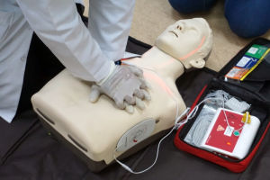 Person performing CPR chest compressions on a training manikin with an automated external defibrillator (AED) in use during a first aid training session.