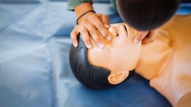 Person practicing CPR rescue breathing on a medical training manikin placed on a blue mat.