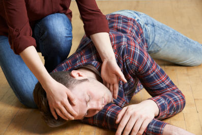 Person assisting an unconscious man lying on the floor, demonstrating the recovery position for first aid.