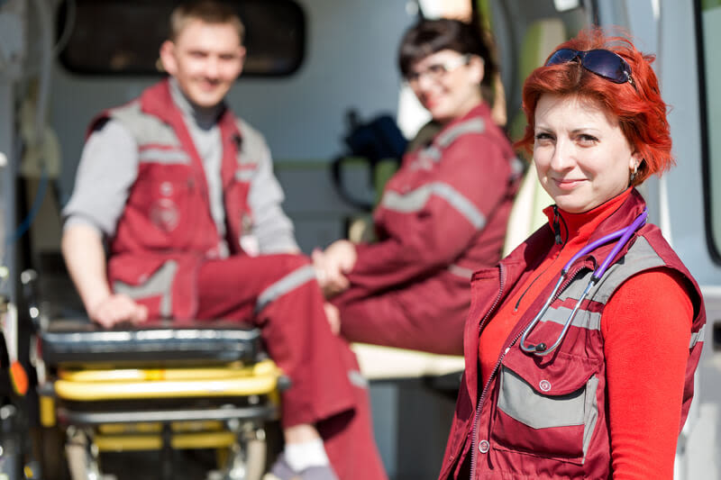 Three medical personnel for BLS, and ALS is standing outside an ambulance setting up a stretcher