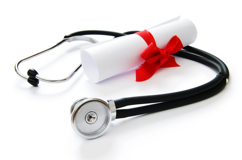 A stethoscope is on a table with a rolled paper tied with a red ribbon that signifies ACLS certificate